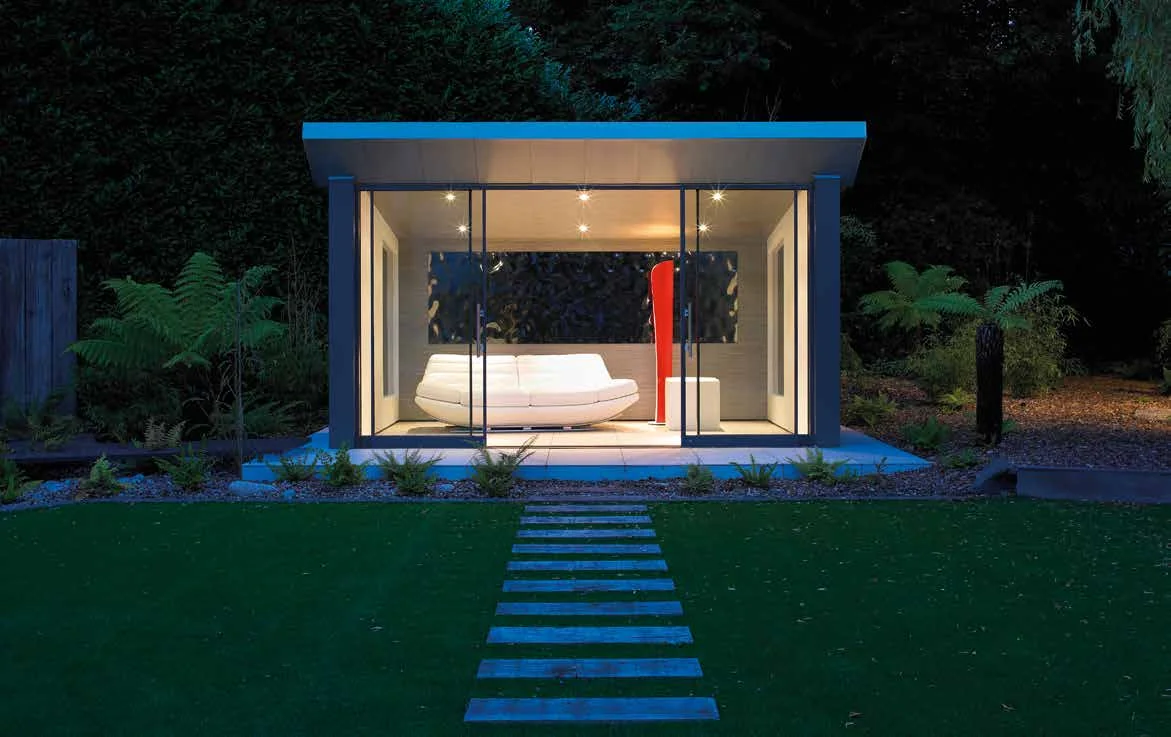 Illuminated garden pavilion with frameless sliding glass doors at dusk