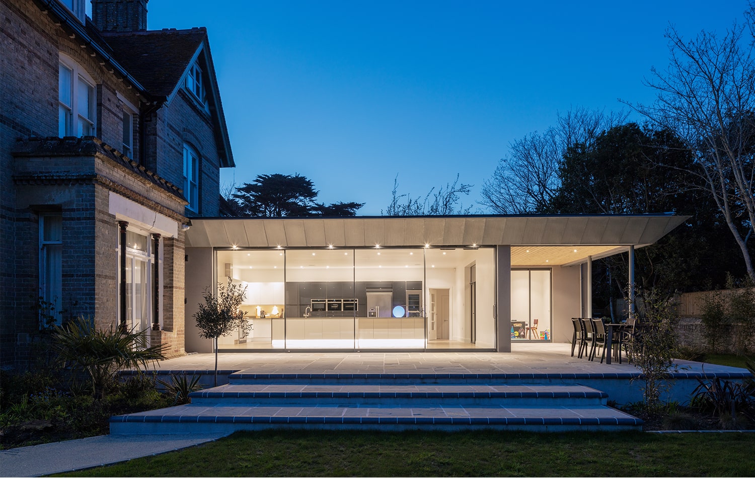 Infiniti frameless sliding doors opening onto an illuminated kitchen at dusk